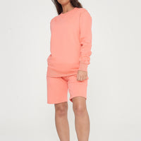 A woman wearing a basic coral sweatshirt and matching shorts, standing front-facing.