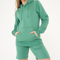 Side view of a woman modeling a green basic hoodie, highlighting fit and sleeve texture.