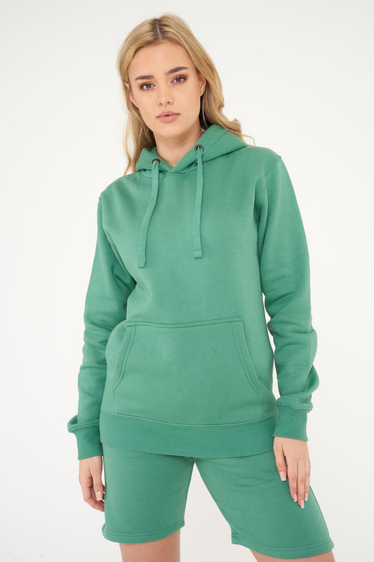 A woman wearing a basic green hoodie with matching shorts, standing in a relaxed pose. 