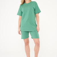 Woman standing in green shorts and t-shirt, casual style pose highlighting color and comfort. 