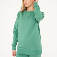 Woman standing in green sweatshirt and shorts, casual pose displaying color and minimalist style. 