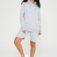 A woman wearing a basic grey hoodie with matching shorts, standing front-facing. 