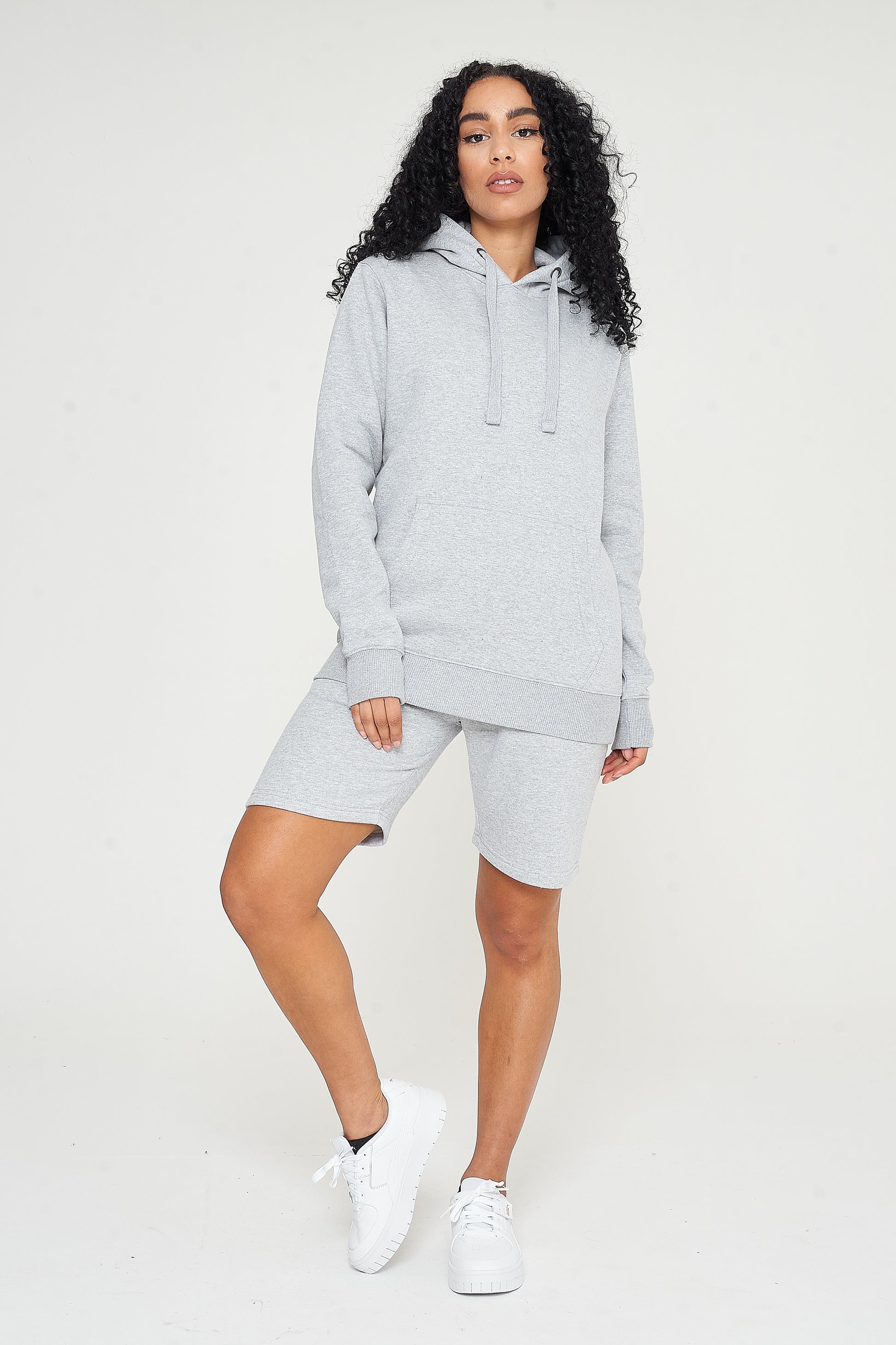 A woman wearing a basic grey hoodie with matching shorts, standing front-facing. 