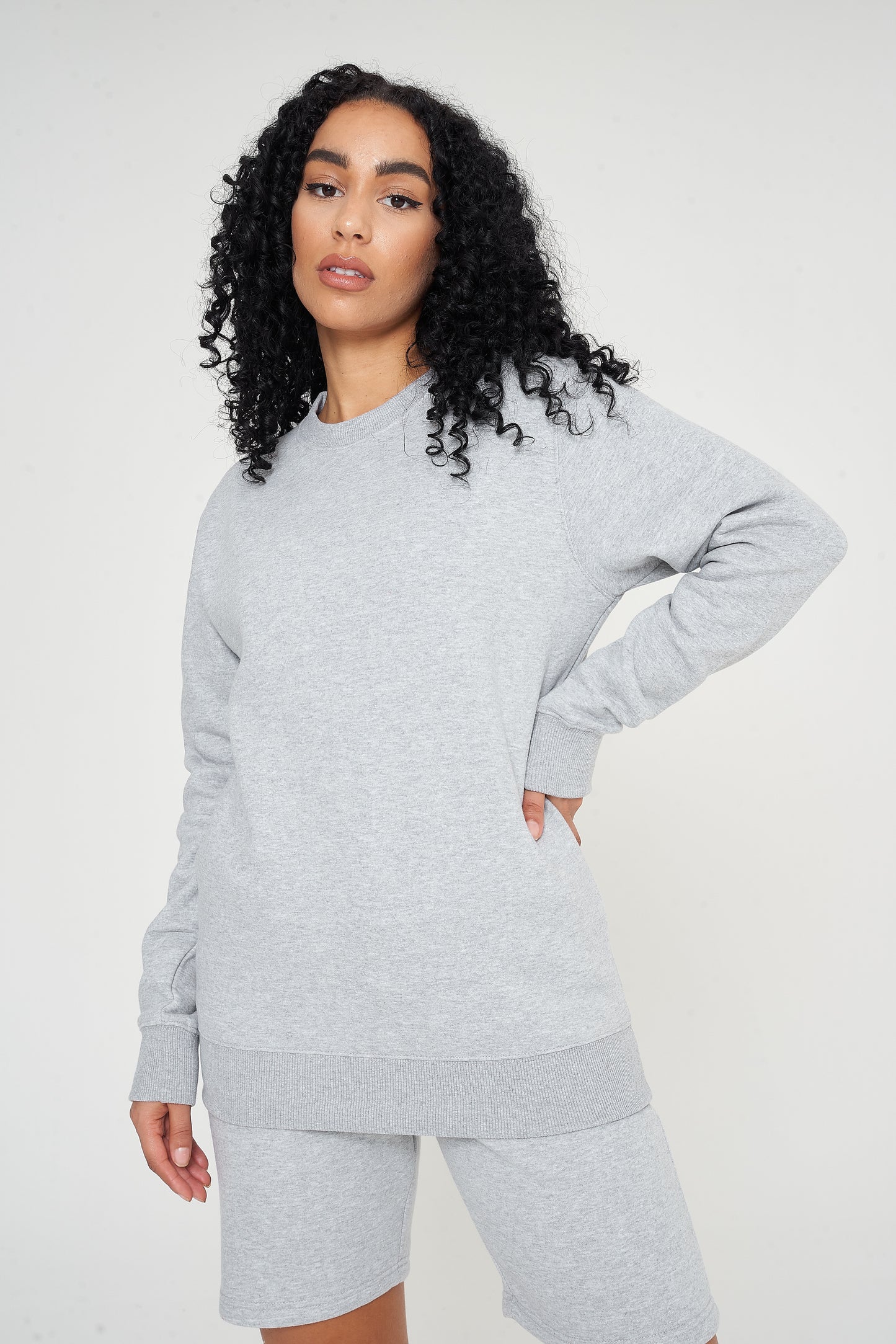 Woman standing in a basic grey sweatshirt and shorts, relaxed side pose.