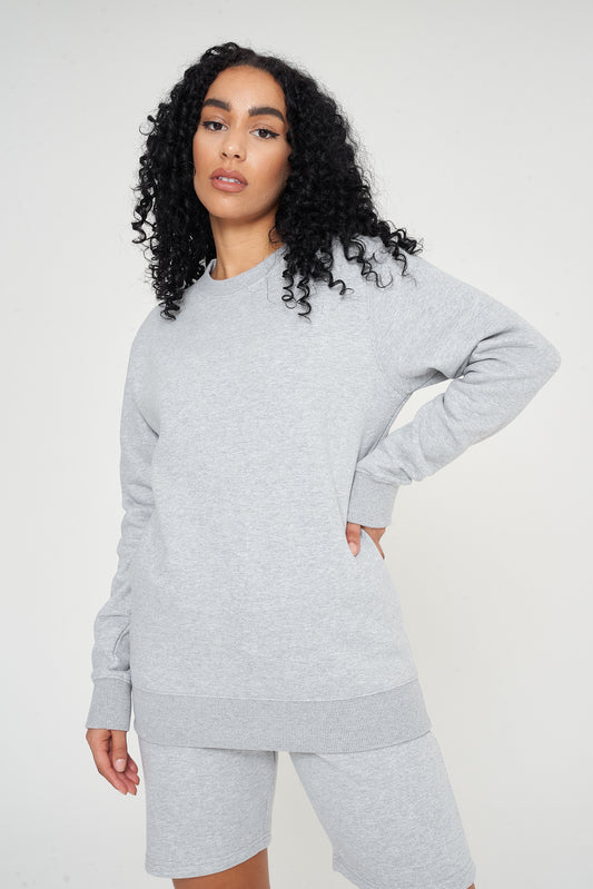 Woman standing in a basic grey sweatshirt and shorts, relaxed side pose.