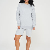 A woman wearing a basic grey sweatshirt with casual shorts, front-facing. 