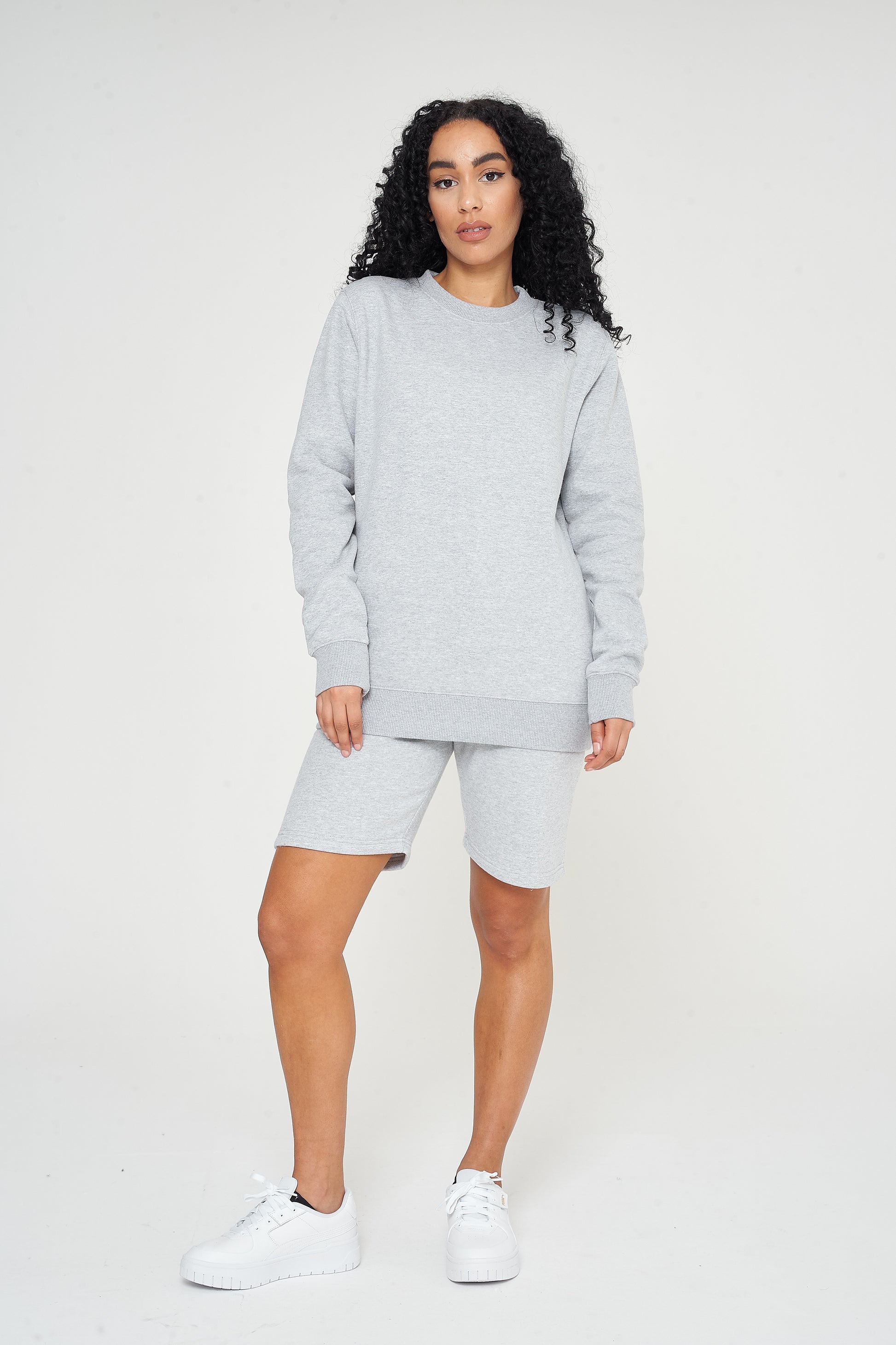 A woman wearing a basic grey sweatshirt with casual shorts, front-facing. 