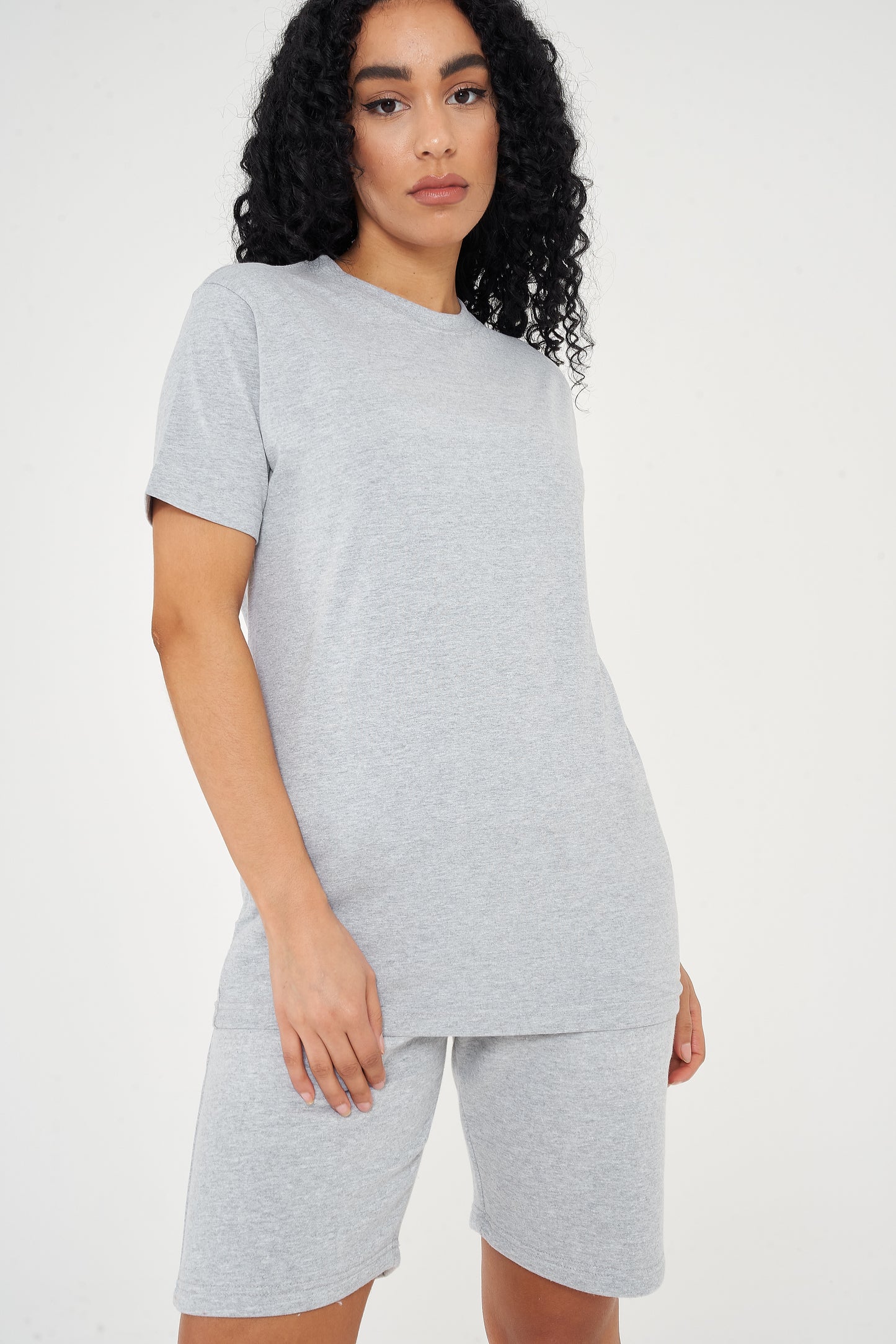A woman standing in a basic grey t-shirt and matching shorts, a casual everyday outfit. 