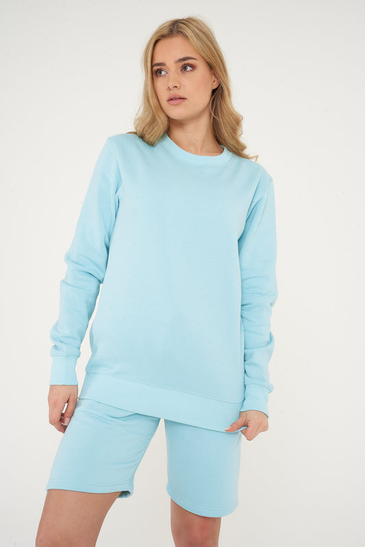 Woman in a turquoise basic sweatshirt and shorts, standing in a casual pose for everyday style.