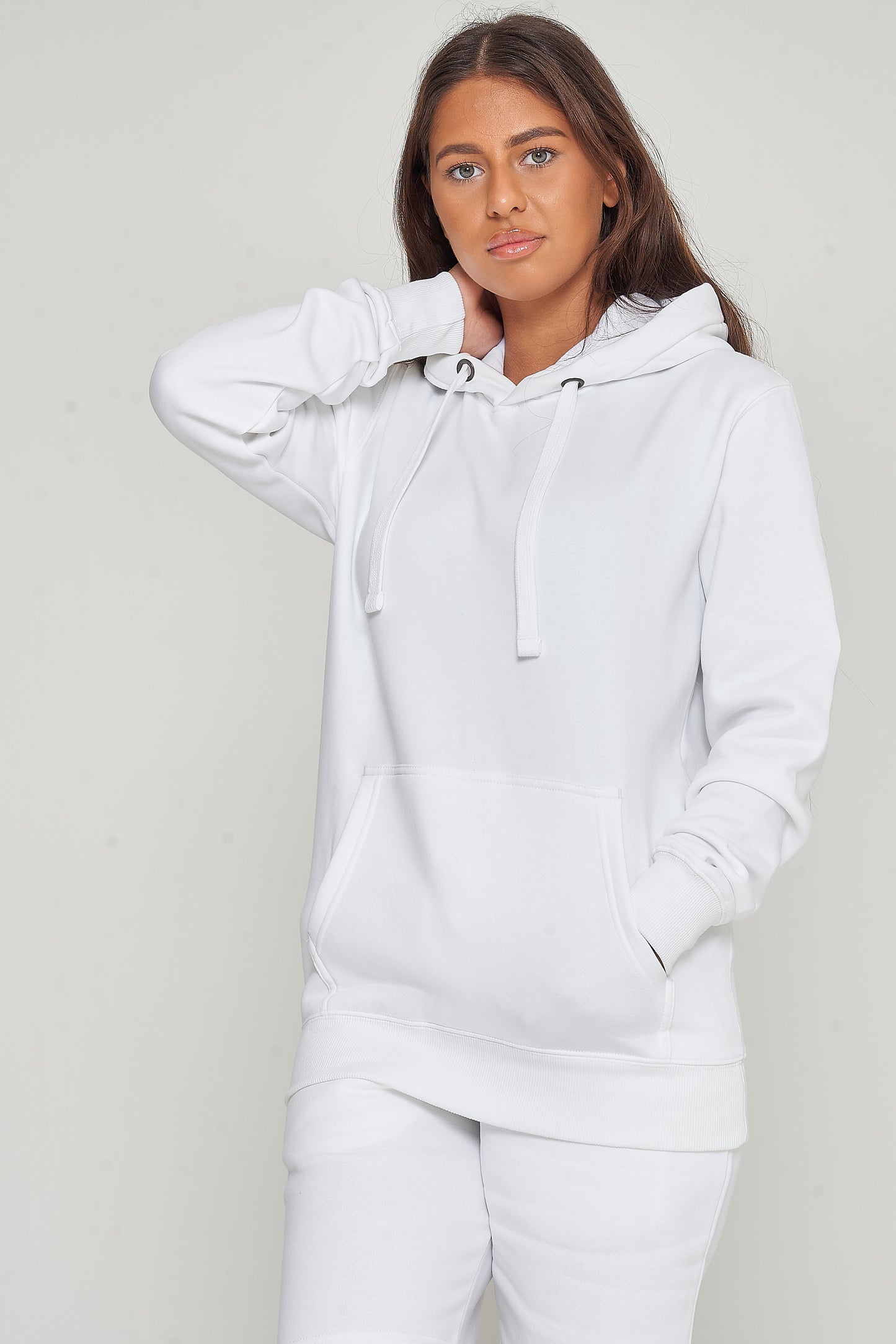 Woman posing in basic white hoodie and shorts, hands in kangaroo pocket, displaying everyday comfort.