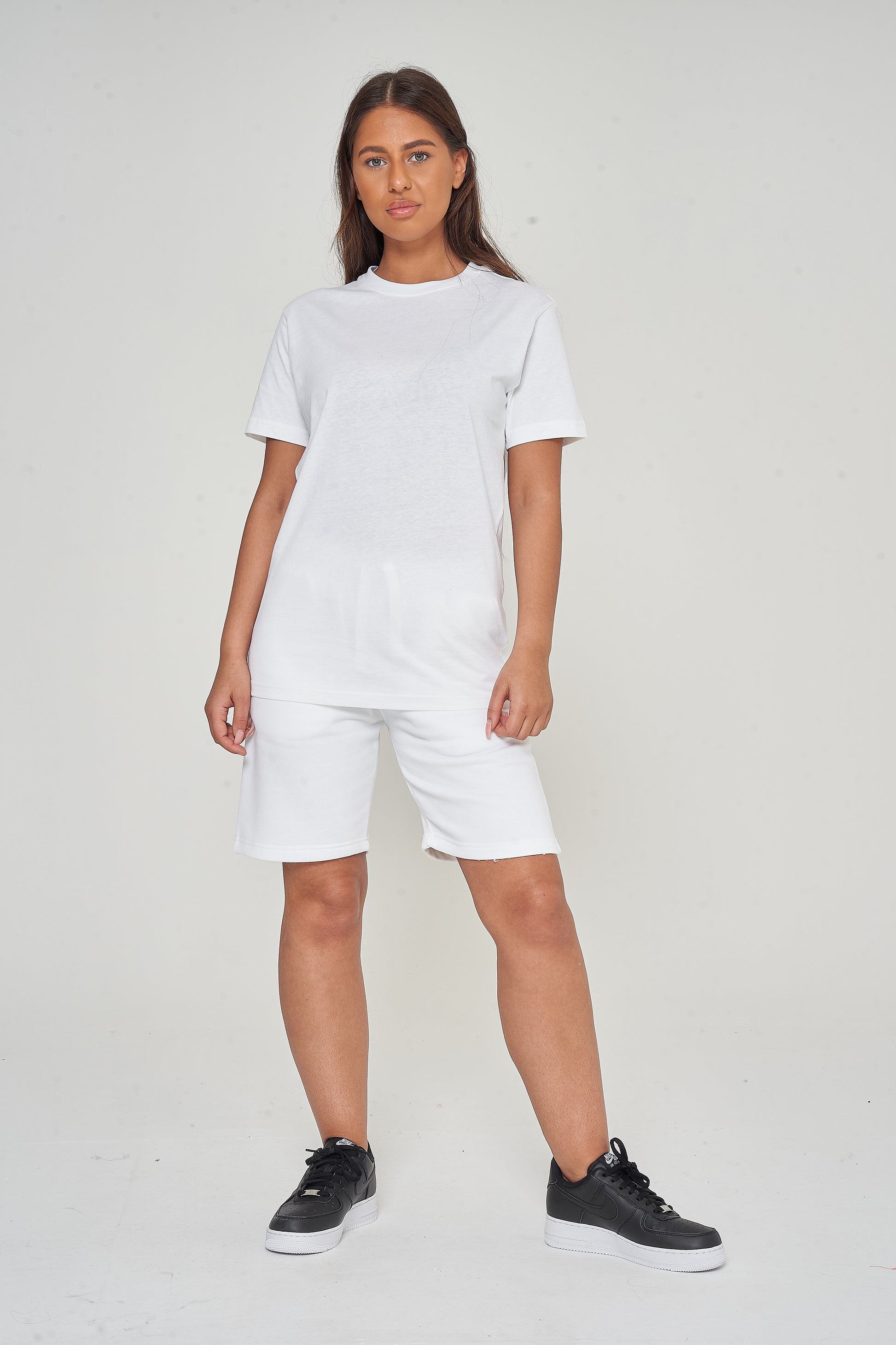 Woman standing in basic white t-shirt and shorts, showing versatile casual look.