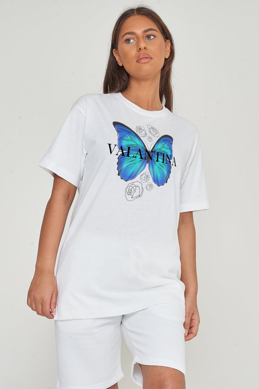 A woman wearing a white oversized T-shirt with a glowing blue butterfly graphic, standing against a plain background.