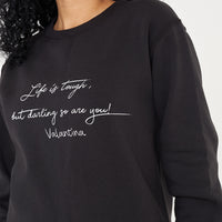 Woman wearing the black Life Is Tough Sweatshirt styled with casual bottoms, highlighting the bold front motivational print and comfortable fit.