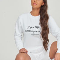 Woman wearing the white Life Is Tough Sweatshirt styled with casual bottoms, highlighting the bold front motivational print and comfortable fit.