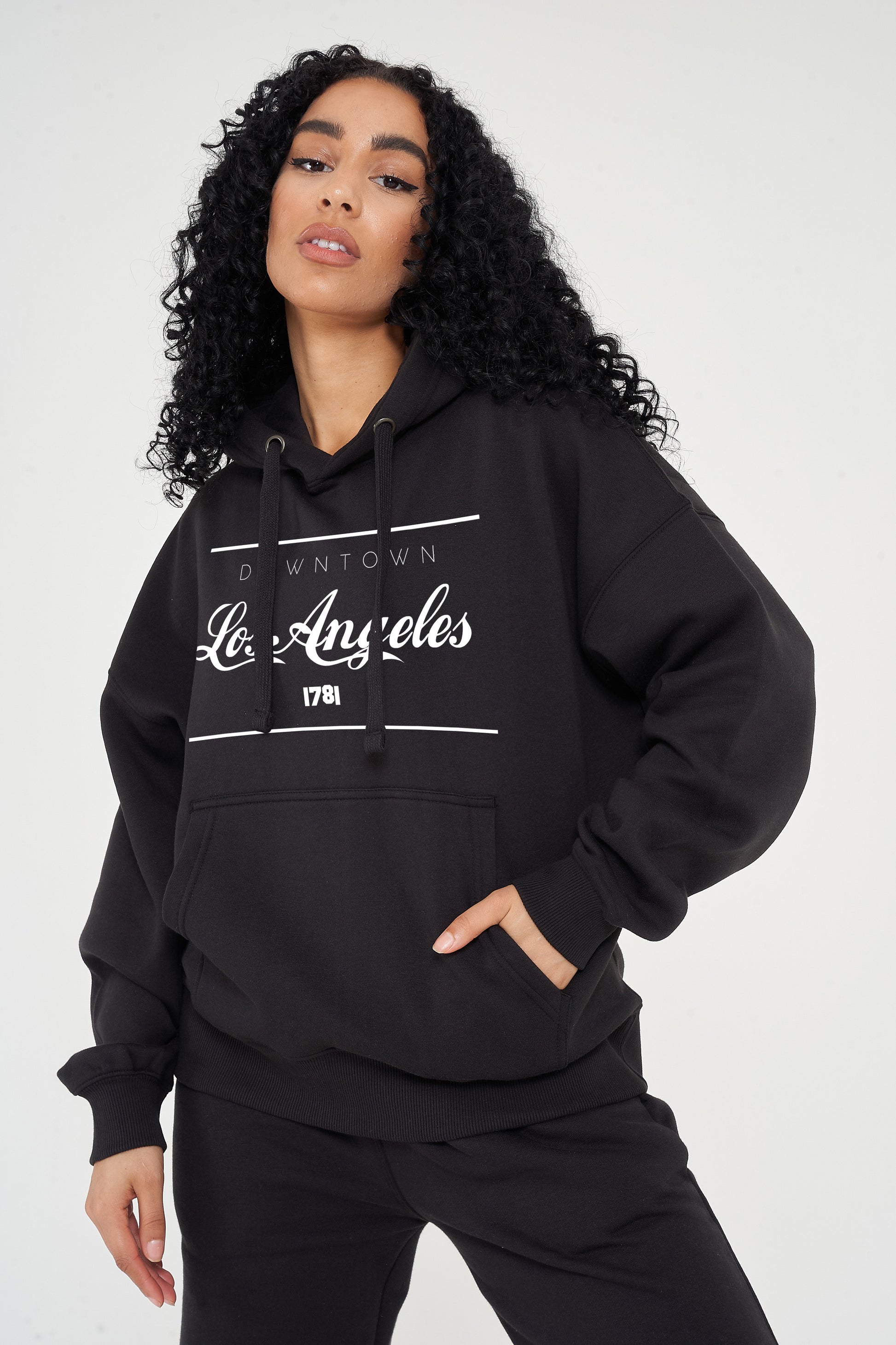 Woman wearing the black Los Angeles Oversized Hoodie styled with casual bottoms, highlighting the prominent front print and comfortable slouchy fit.
