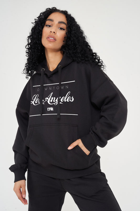 Woman wearing the black Los Angeles Oversized Hoodie styled with casual bottoms, highlighting the prominent front print and comfortable slouchy fit.