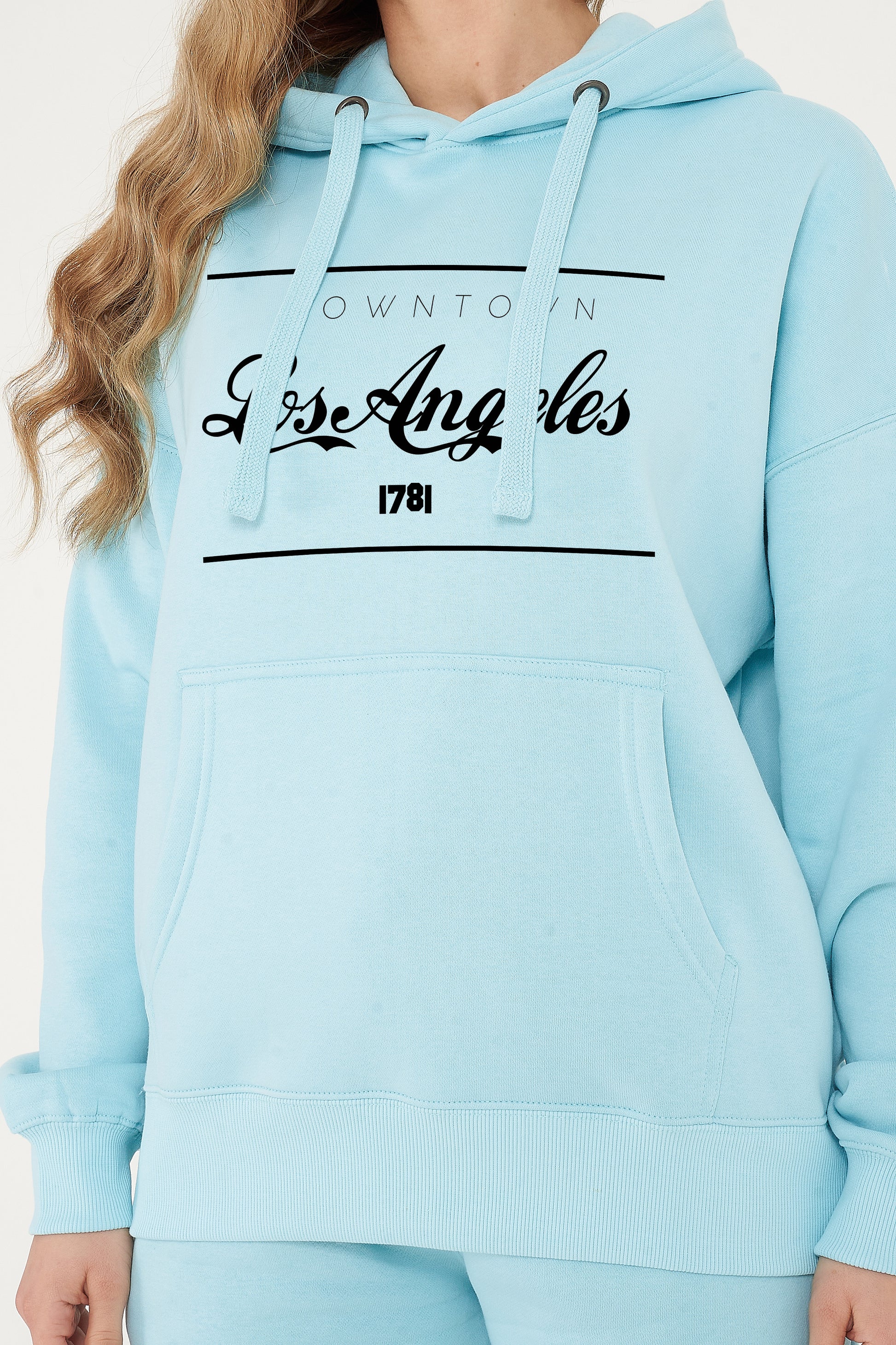 Woman wearing the turquoise Los Angeles Oversized Hoodie styled with casual bottoms, highlighting the bold front print and comfortable oversized fit.