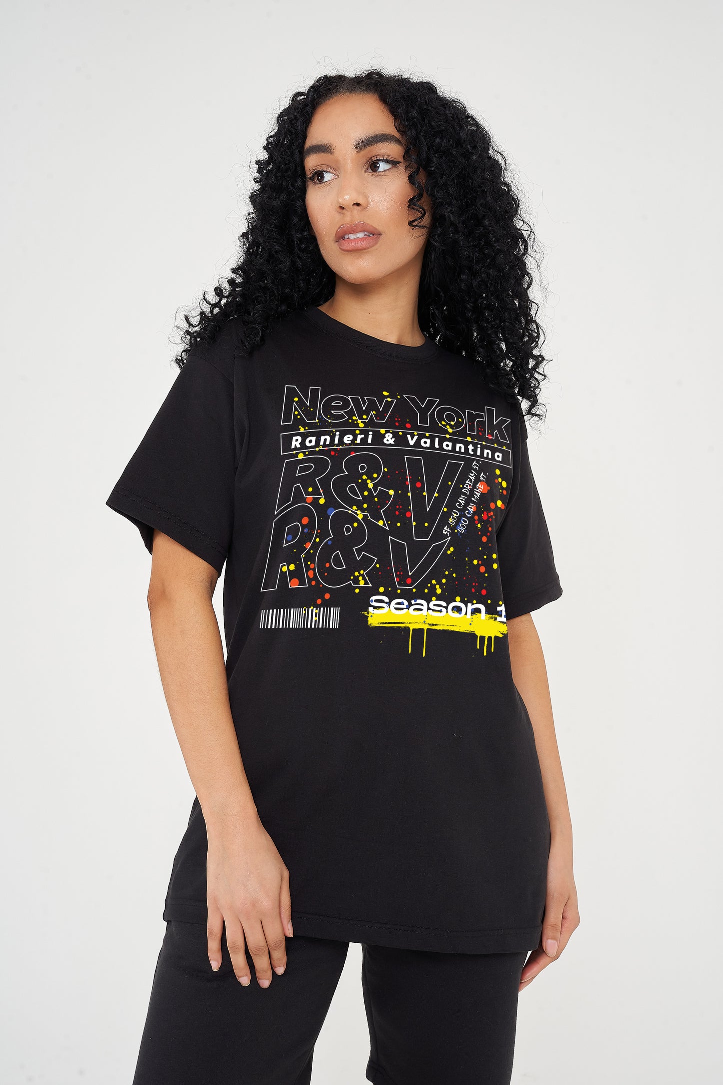 Woman wearing the black New York Season 1 Oversized T-Shirt styled with casual bottoms, highlighting the front graphic and comfortable oversized fit.