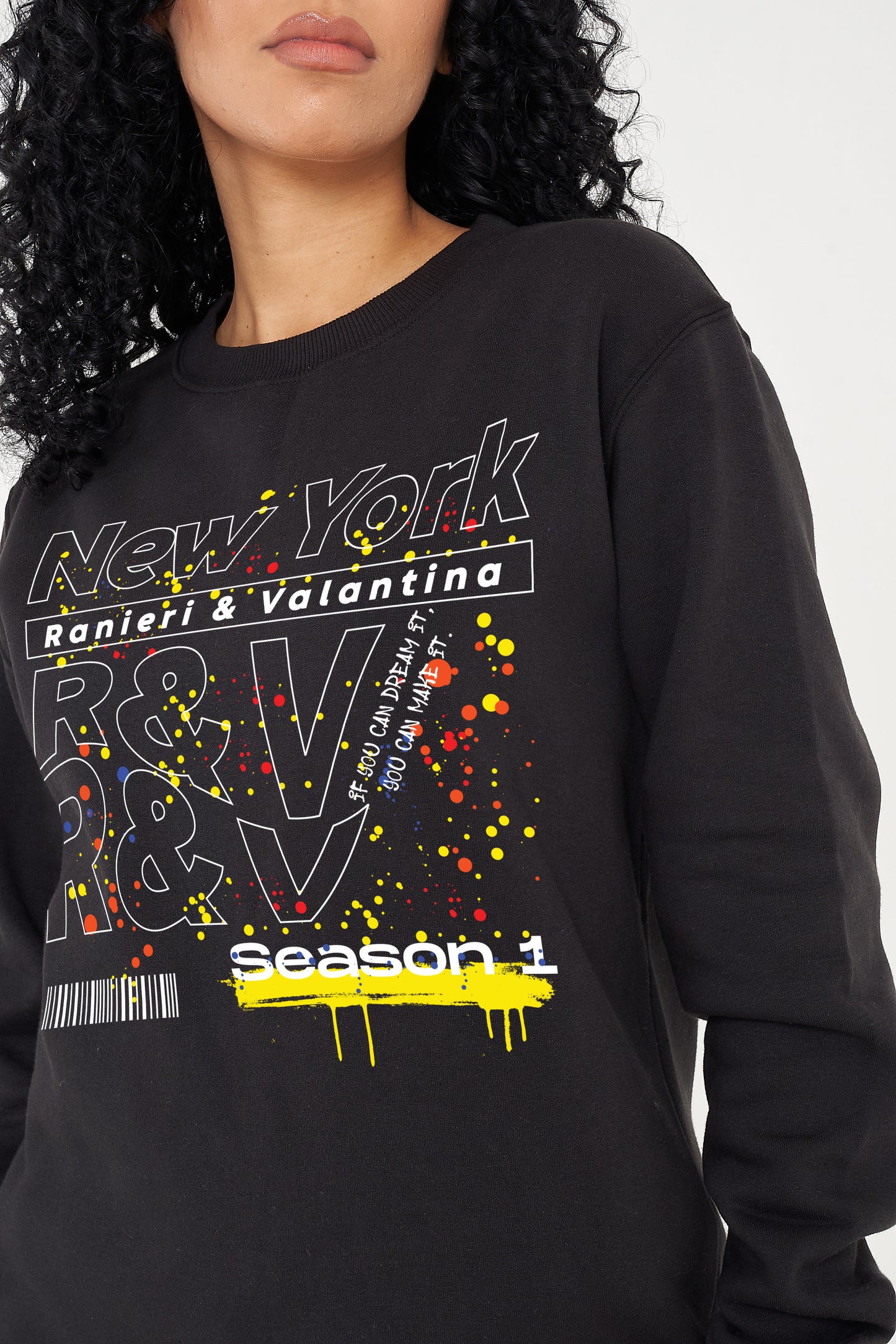Woman wearing the black New York Season 1 Sweatshirt styled with casual bottoms, highlighting the prominent front graphic and comfortable oversized fit.