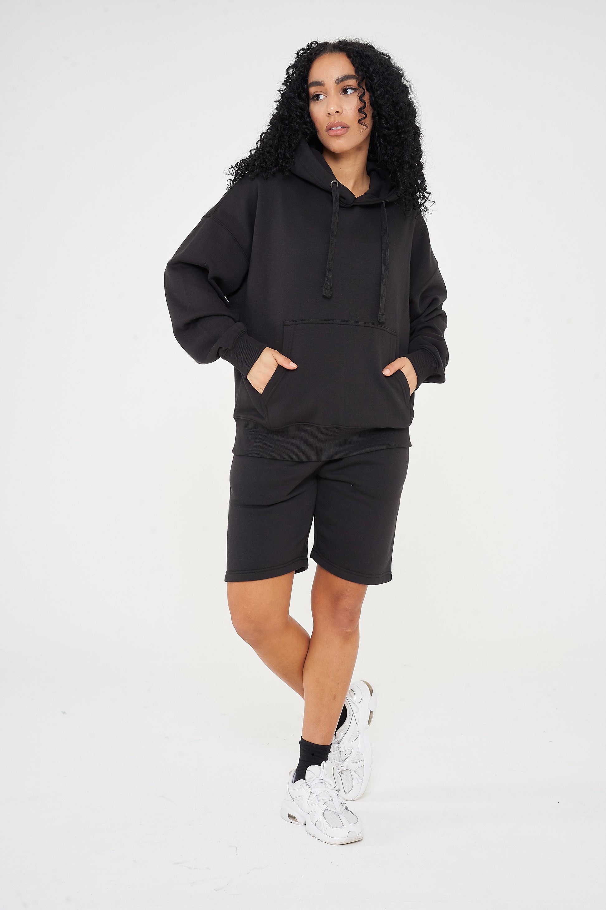 A woman wearing an oversized black hoodie and shorts, standing front-facing, showing a loose fit. 