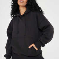 Woman in oversized black hoodie with hands in pocket, showing relaxed streetwear look. 