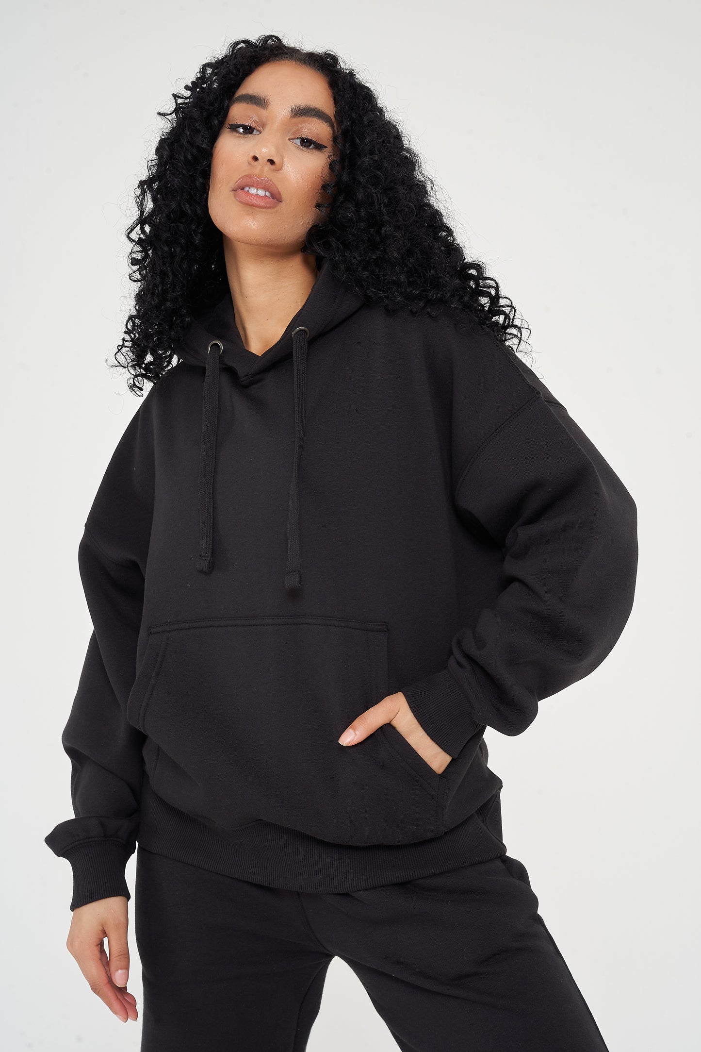 Woman in oversized black hoodie with hands in pocket, showing relaxed streetwear look. 