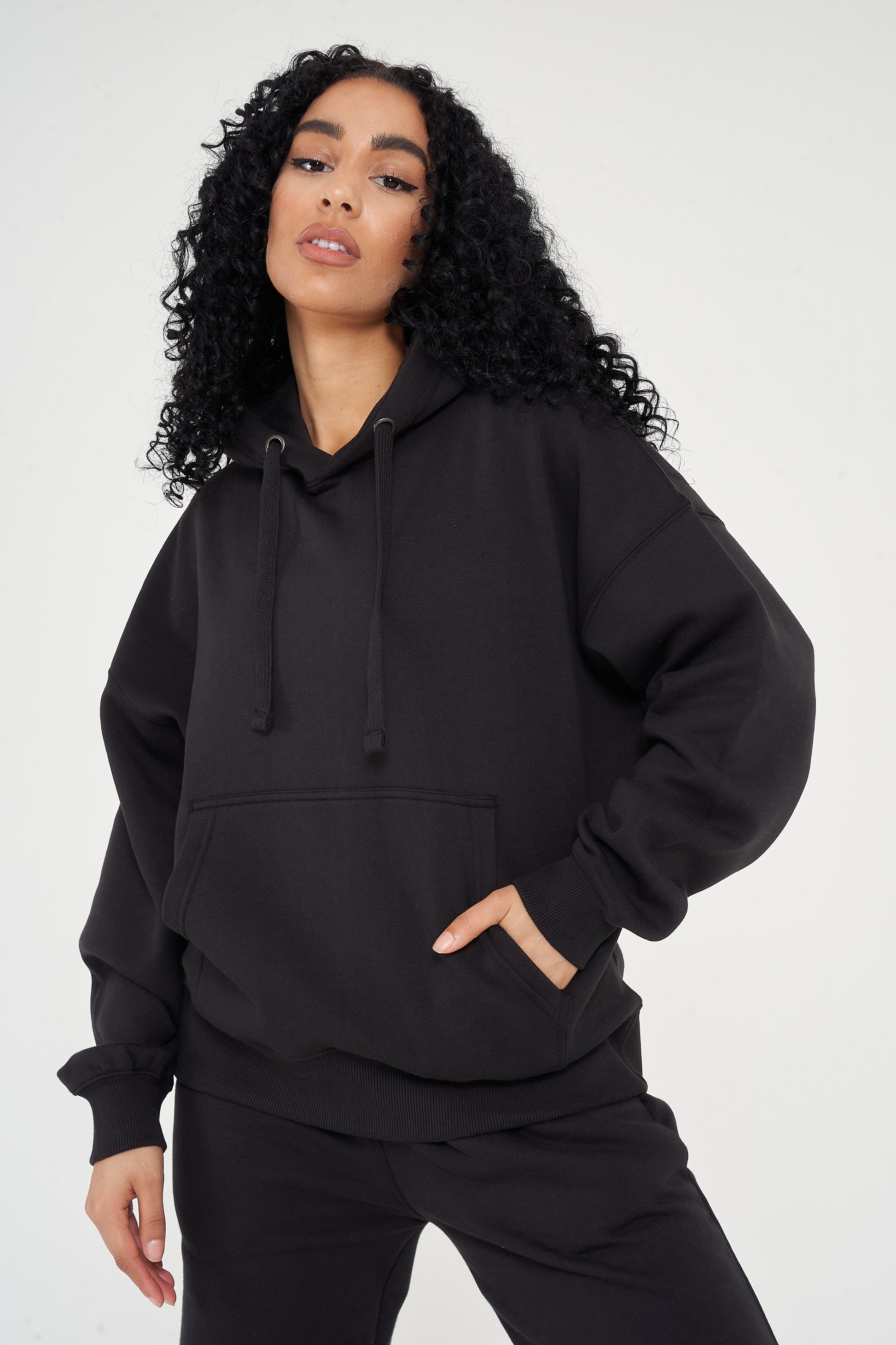 Woman in oversized black hoodie with hands in pocket, showing relaxed streetwear look. 