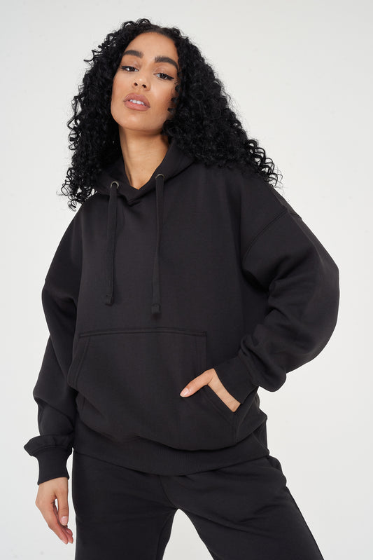 Woman in oversized black hoodie with hands in pocket, showing relaxed streetwear look. 