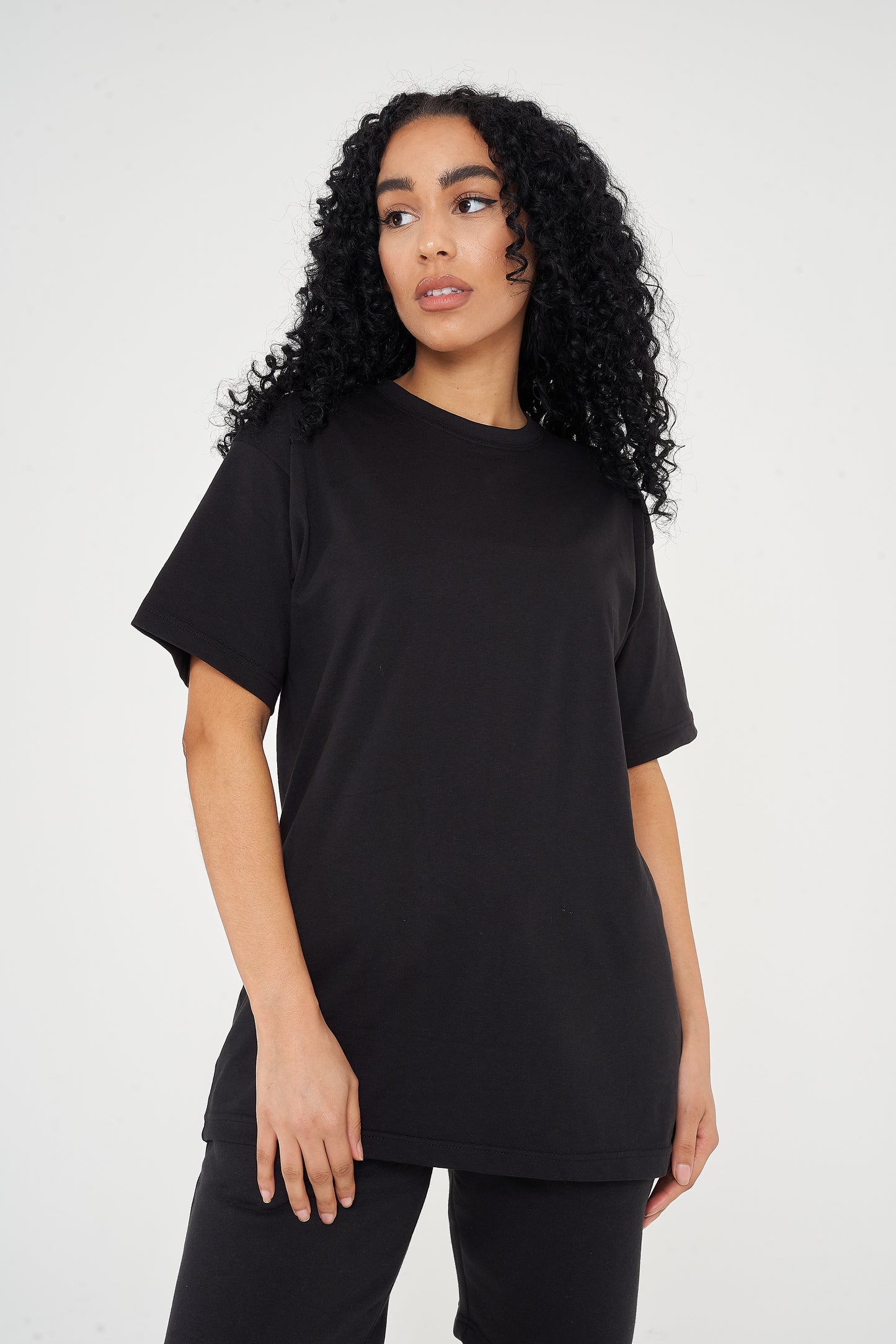 A woman standing in an oversized black t-shirt, displaying a side profile and length.