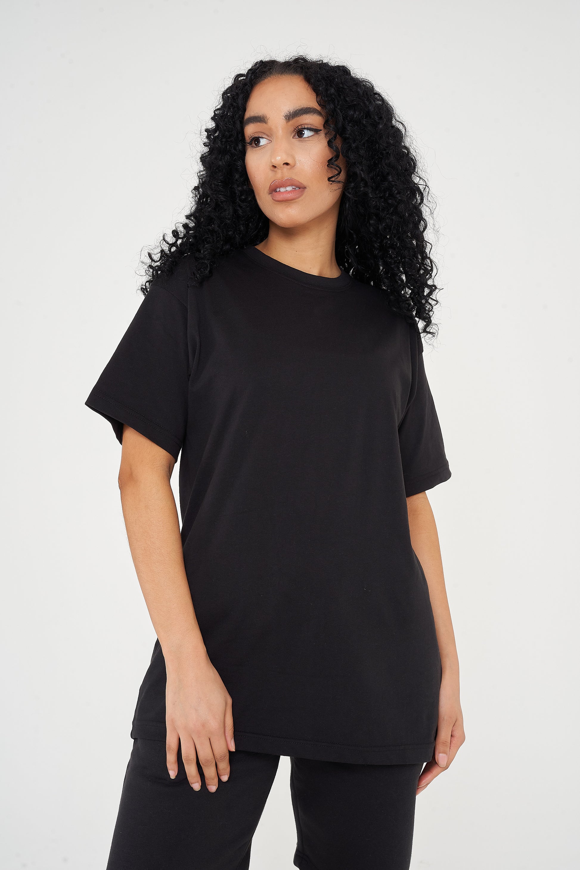 A woman standing in an oversized black t-shirt, displaying a side profile and length.