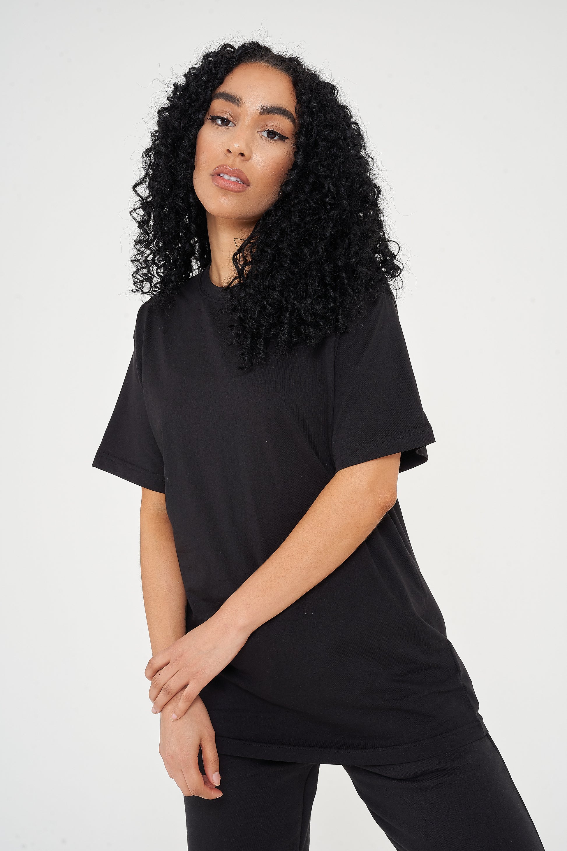 Woman wearing oversized black t-shirt and casual shorts, front view highlighting loose silhouette. 