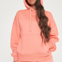 Woman in oversized coral hoodie and matching shorts, posing with hood up to show cozy style. 