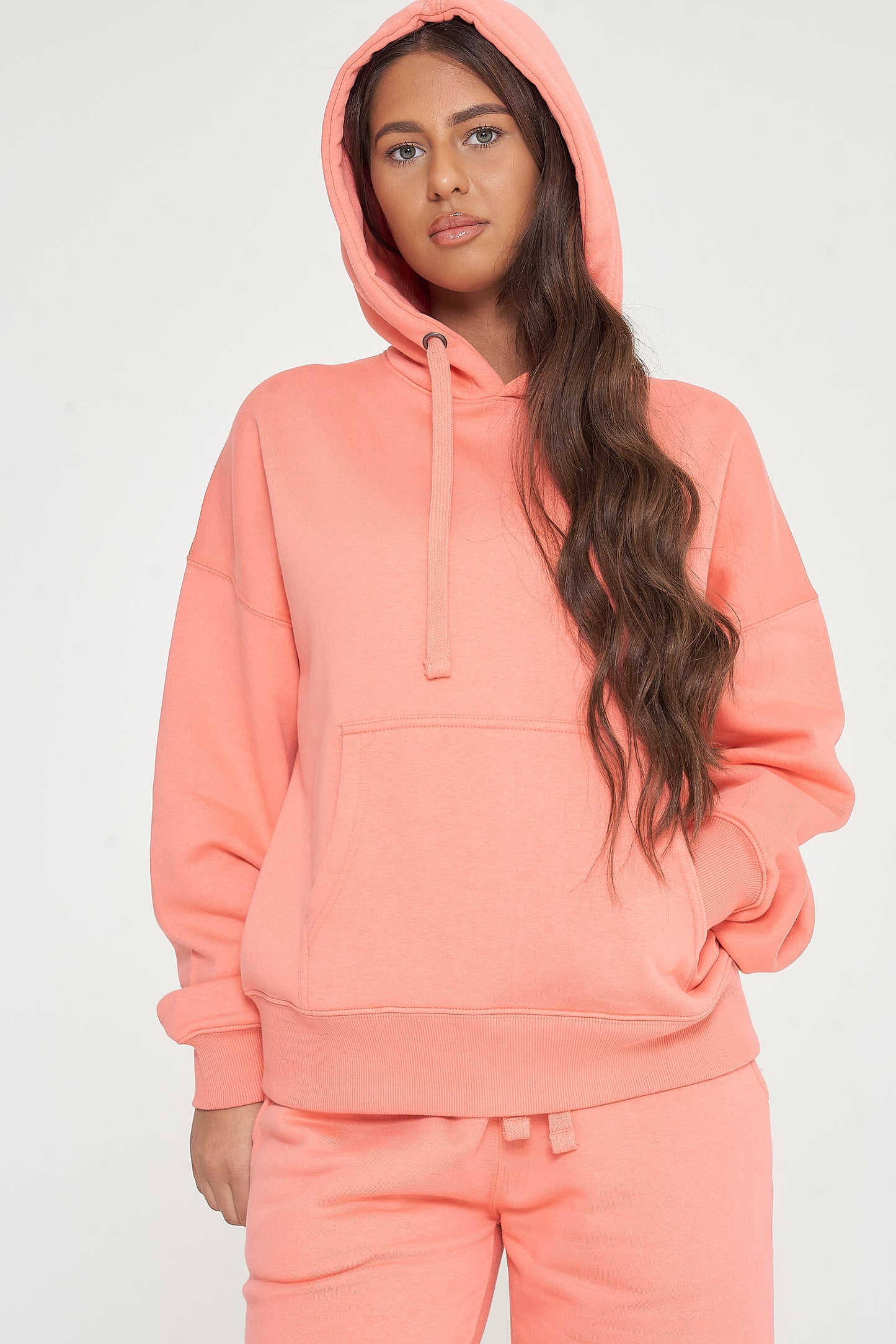 Woman in oversized coral hoodie and matching shorts, posing with hood up to show cozy style. 