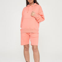Woman wearing oversized coral hoodie and matching shorts, front-facing pose. 