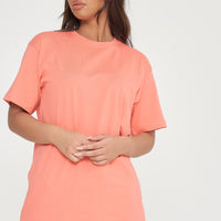 Woman modeling oversized coral t-shirt and shorts, side view showing loose fit. 