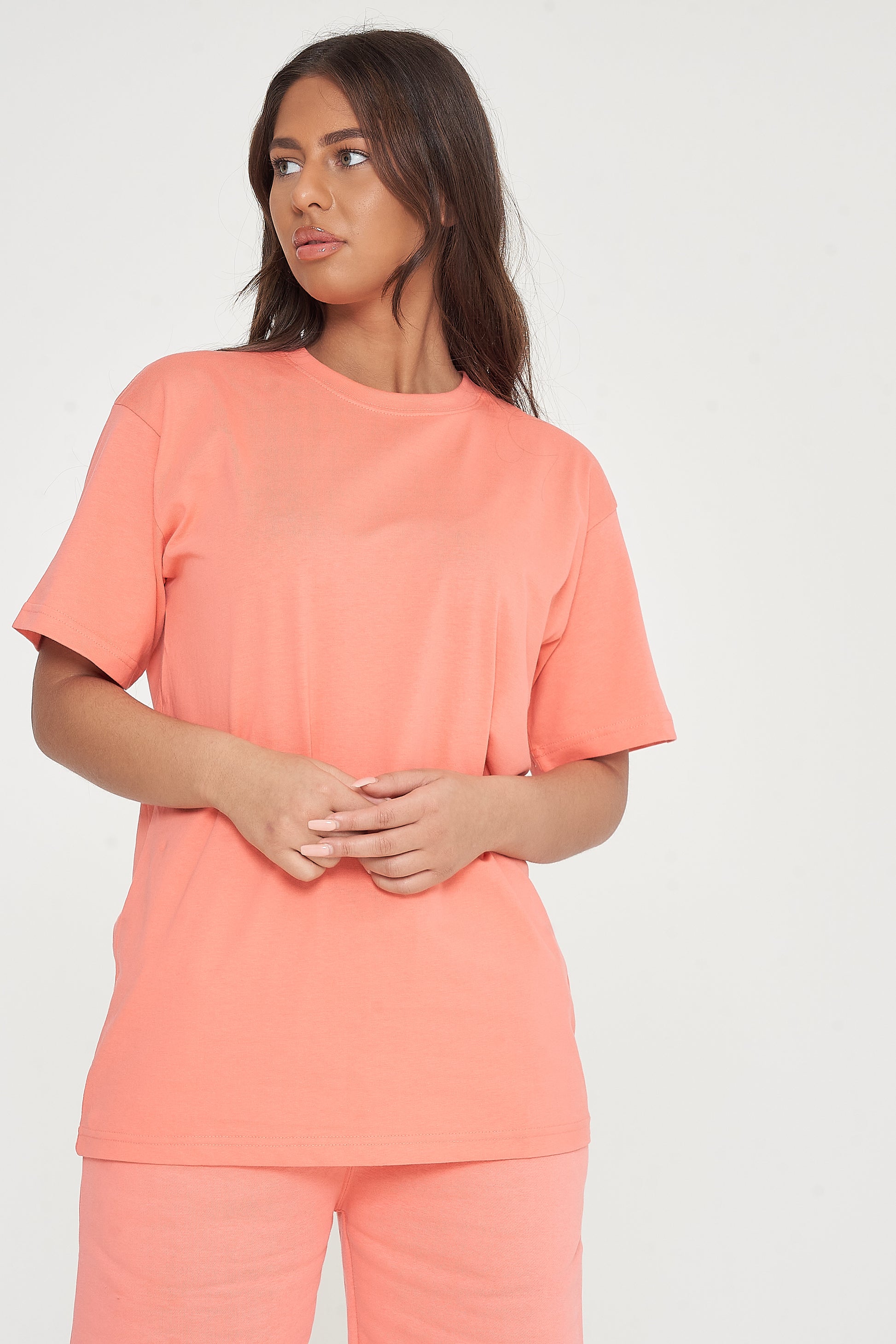 Woman modeling oversized coral t-shirt and shorts, side view showing loose fit. 