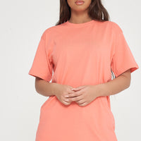 Woman standing in oversized coral t-shirt and shorts, casual pose highlighting color and style. 