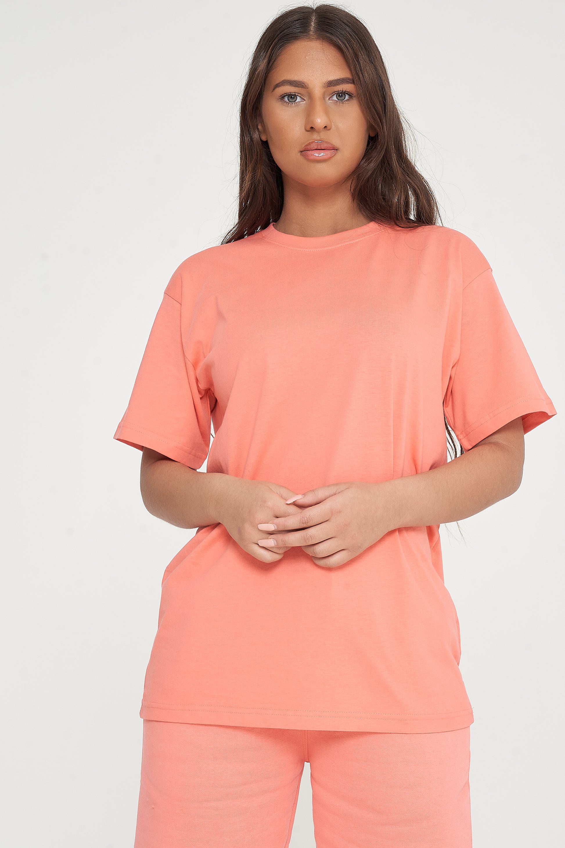 Woman standing in oversized coral t-shirt and shorts, casual pose highlighting color and style. 