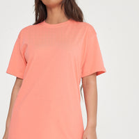 A woman wearing an oversized coral t-shirt and matching shorts, standing front-facing. 