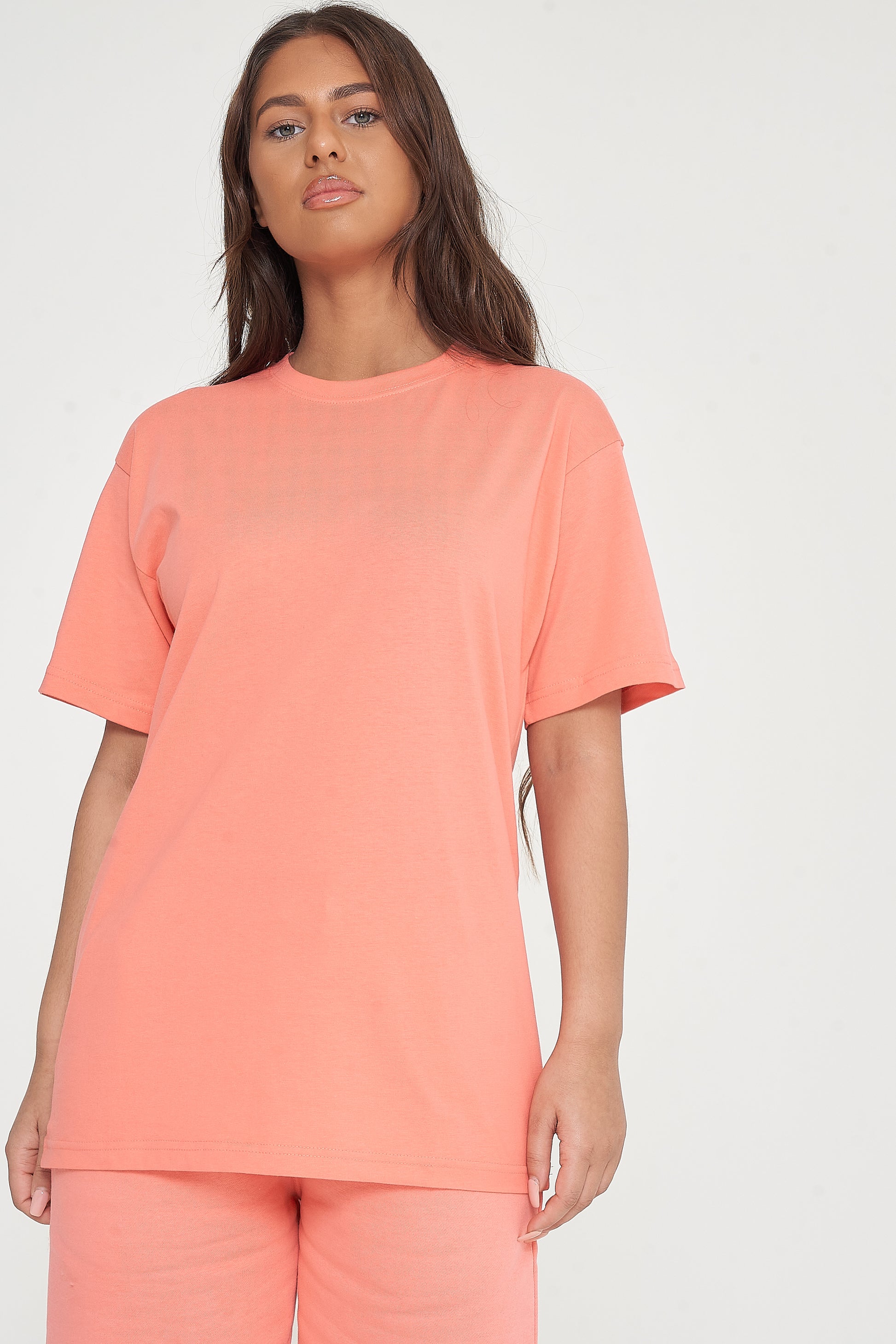 A woman wearing an oversized coral t-shirt and matching shorts, standing front-facing. 