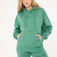 A woman wearing an oversized green hoodie and matching shorts, standing front-facing. 