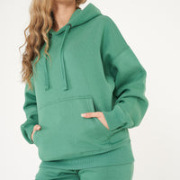 Side view of a woman in an oversized green hoodie and shorts, showing relaxed fit and ribbed cuffs. 