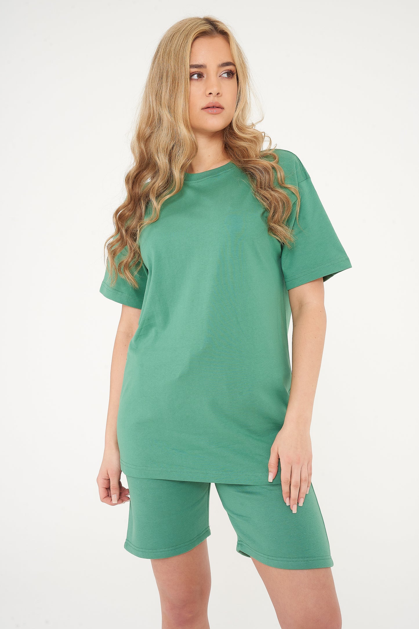 Woman standing in oversized green t-shirt and shorts, casual pose highlighting color and comfort. 