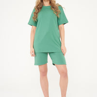 A woman wearing an oversized green t-shirt and matching shorts, standing front-facing. 