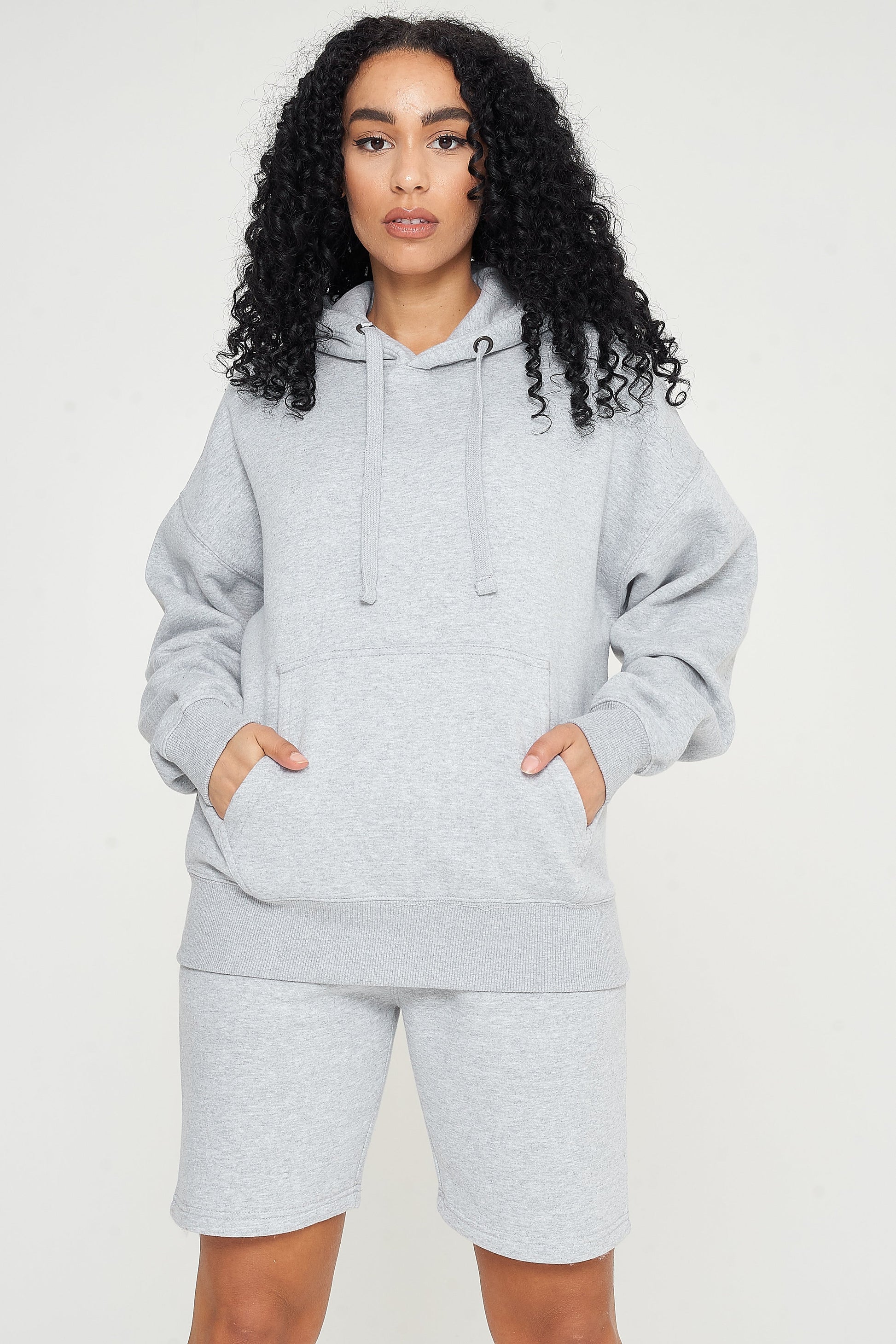 Woman standing in a grey oversized hoodie and shorts, casual pose for versatile styling.