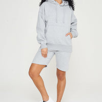 Woman wearing a grey oversized hoodie with matching shorts, front view. 