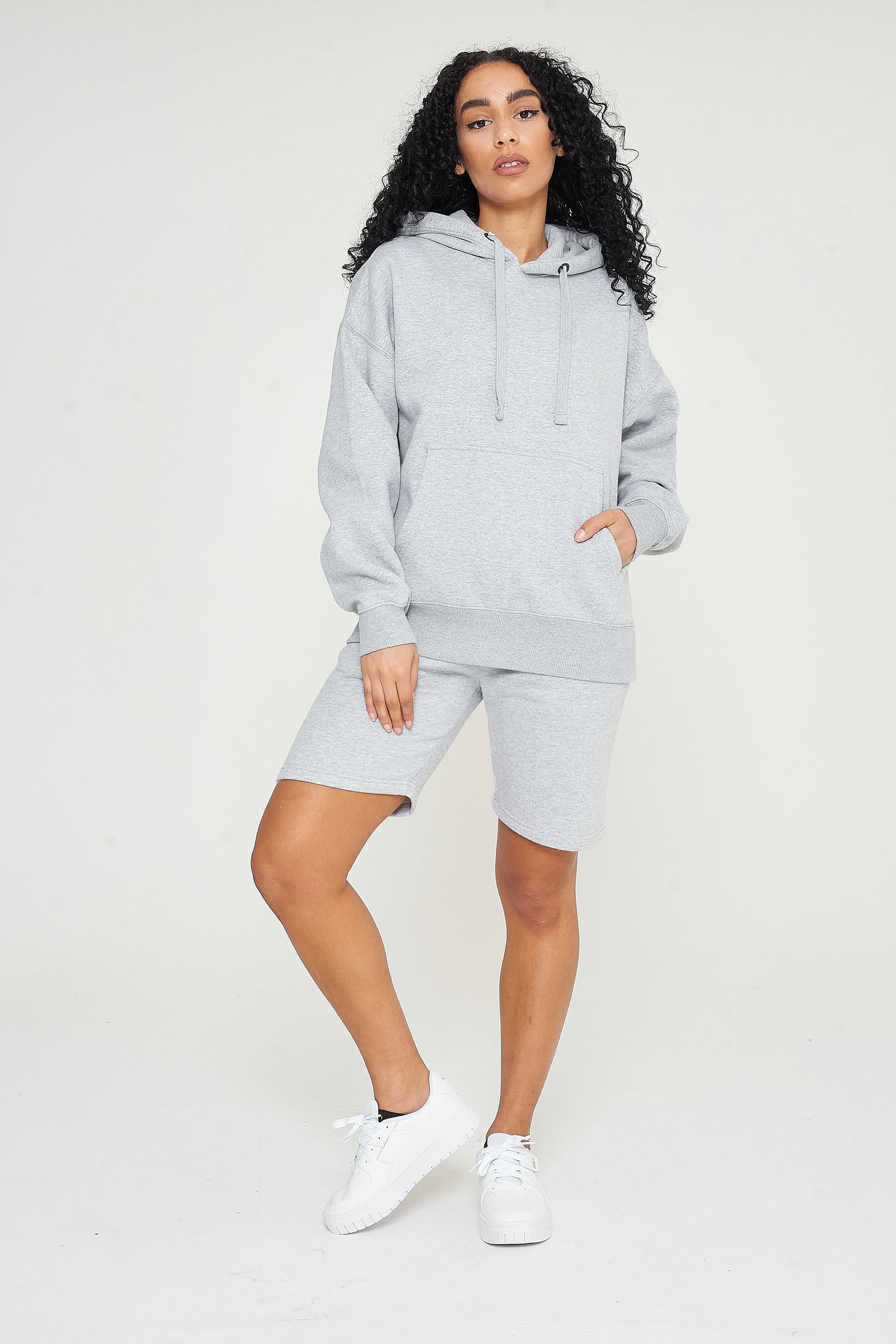 Woman wearing a grey oversized hoodie with matching shorts, front view. 