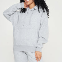 Woman modeling a grey oversized hoodie, side pose showing relaxed silhouette.