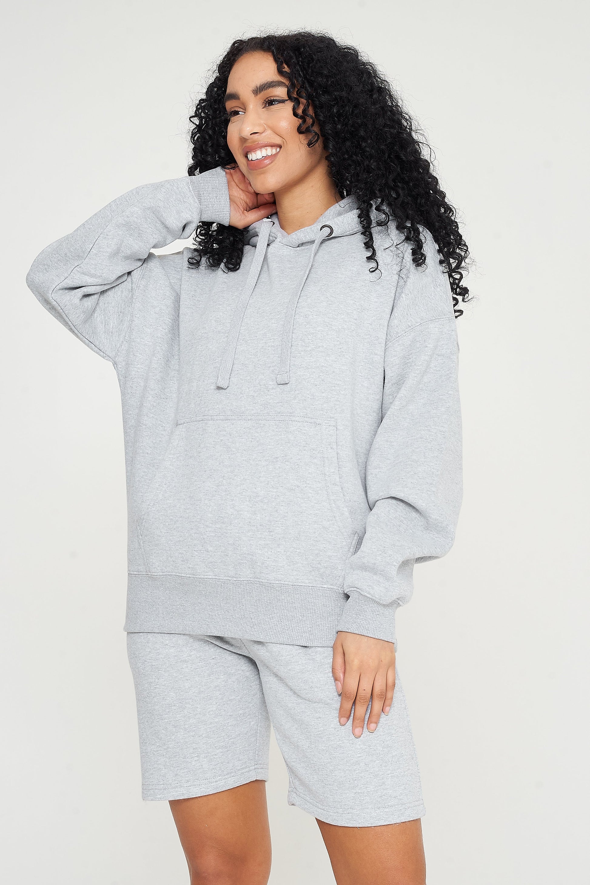 Woman modeling a grey oversized hoodie, side pose showing relaxed silhouette.