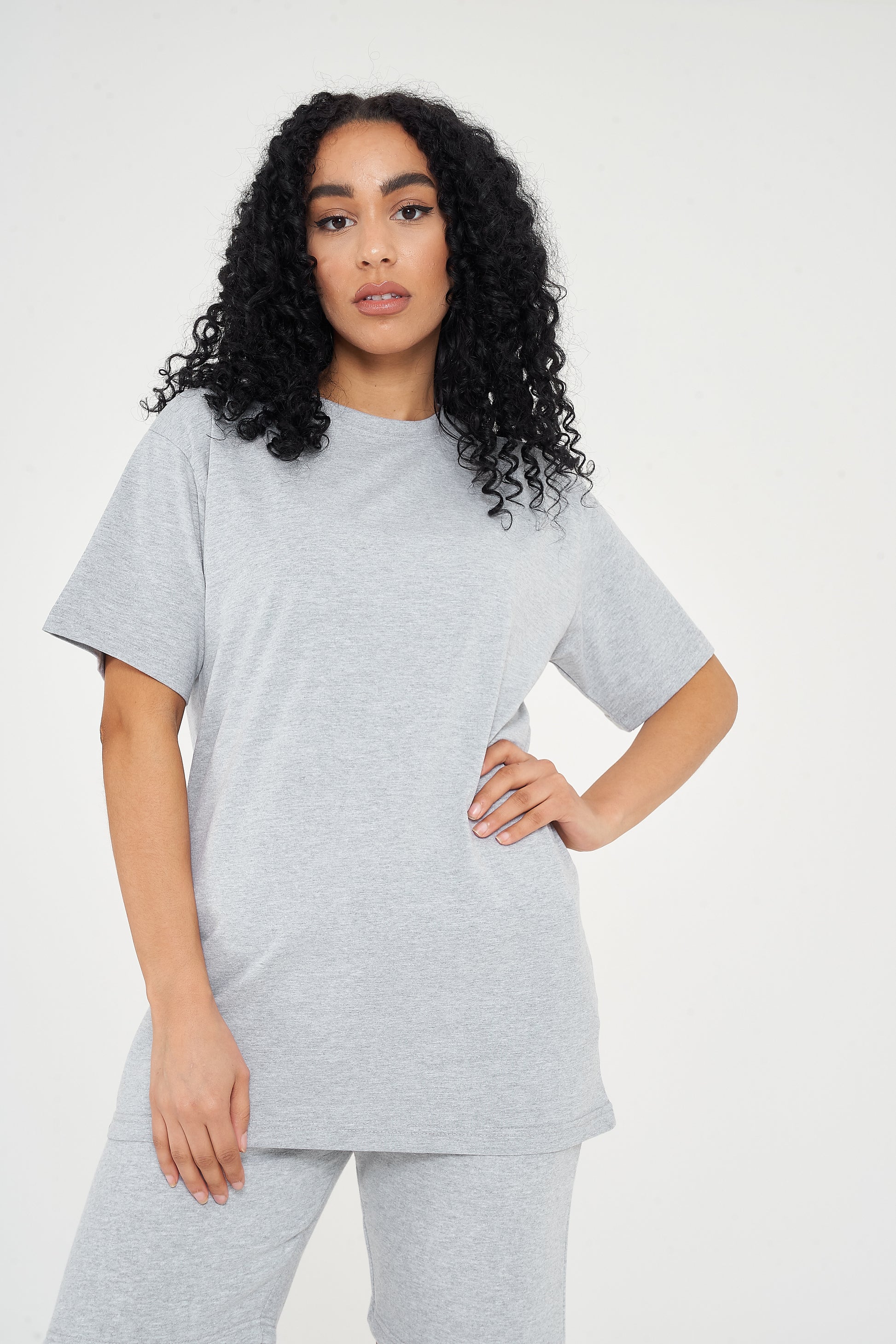 Woman modeling oversized grey t-shirt in a standing side pose, showing relaxed silhouette. 